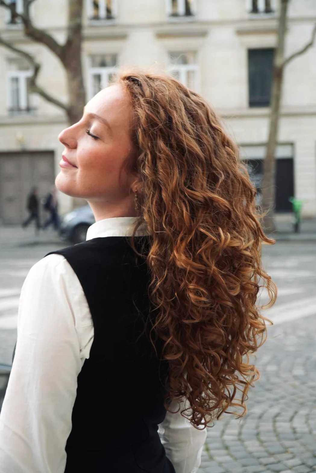 Flo de profil, les yeux fermés, ses longues boucles rousses sur l’épaule, dans une rue de Paris.
