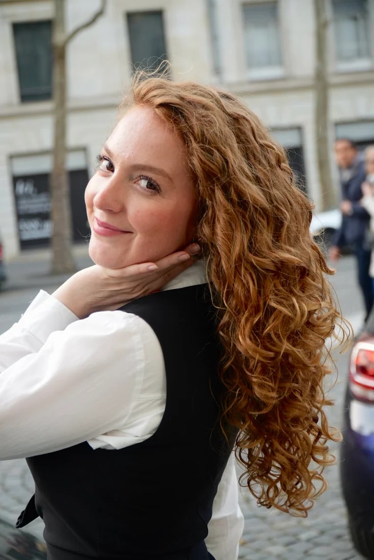 Flo sourit, le menton posé sur la main, ses boucles rousses sur l’épaule.